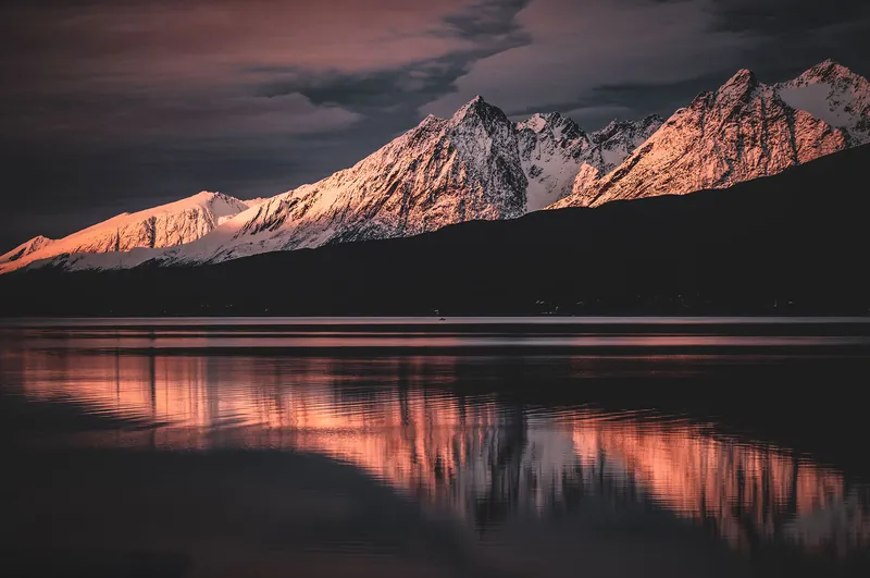 Peaks in pink evening light mirrored in the fjord