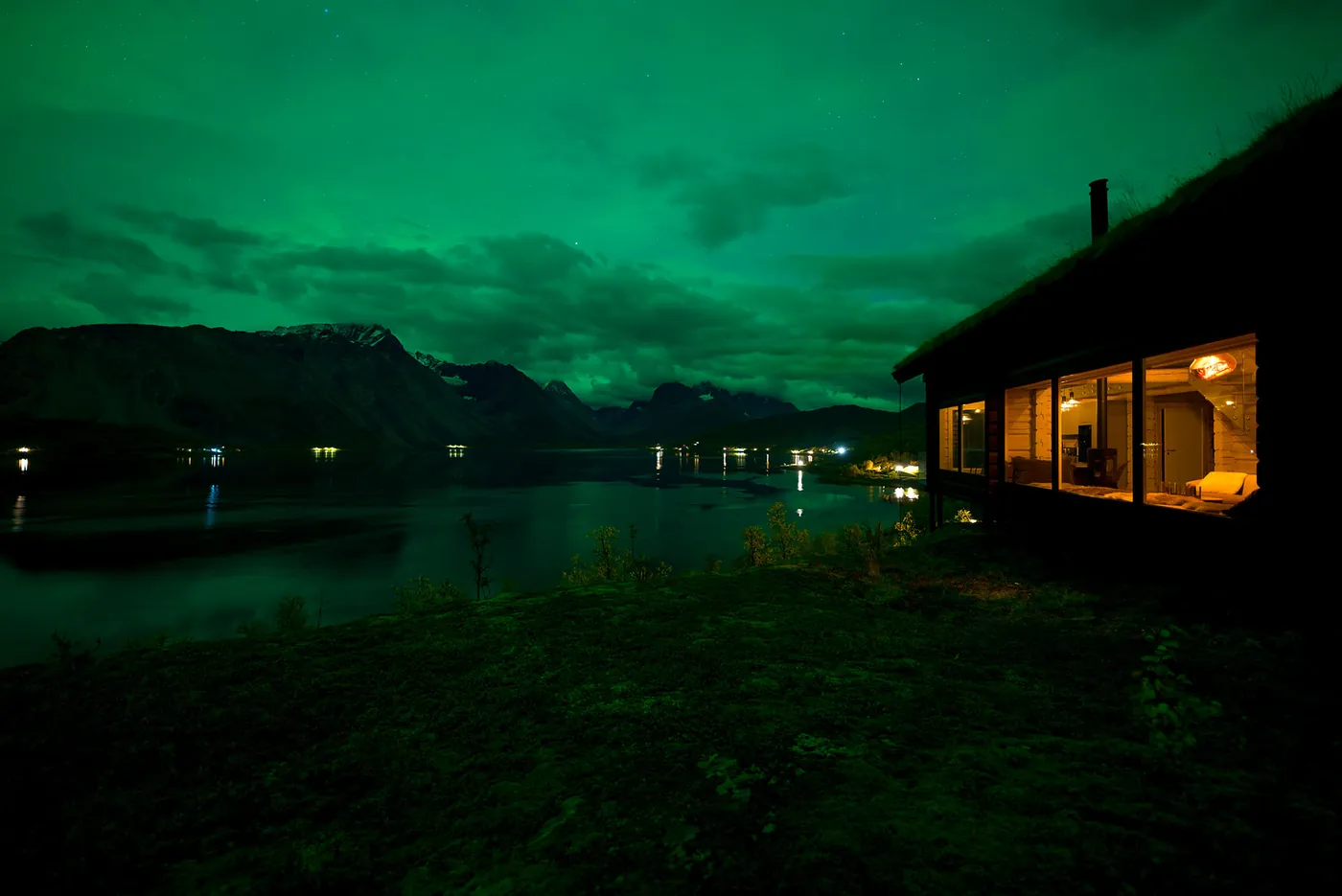 Chalet with lit windows under green northern lights